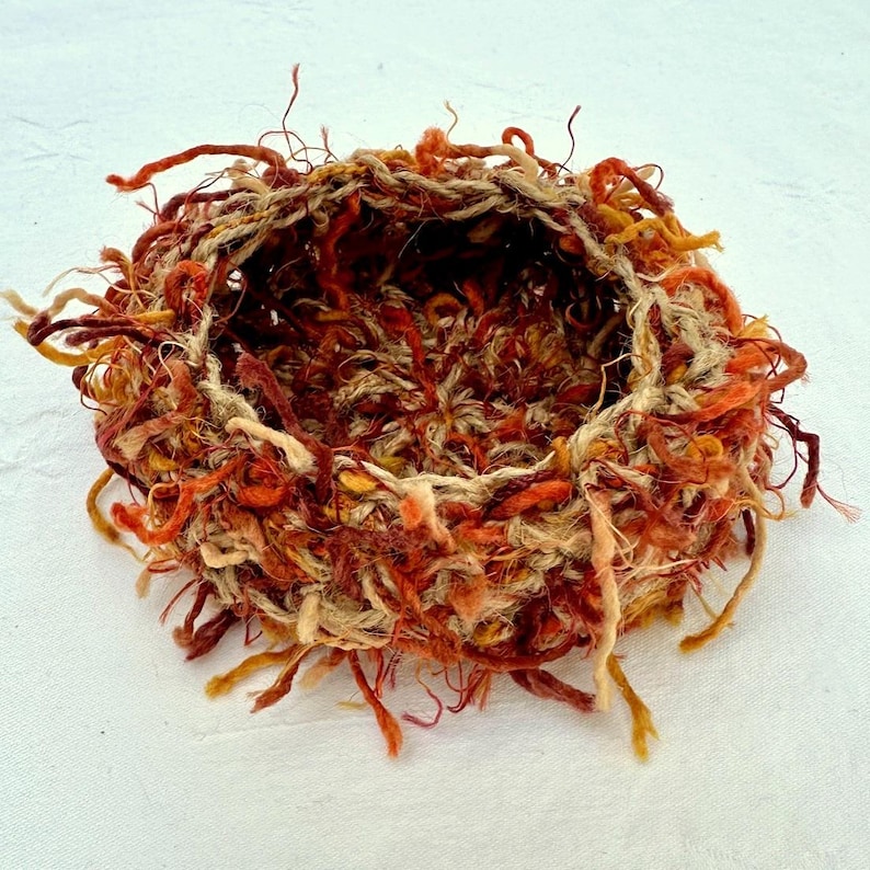 Peut inclure: Un petit panier rond en osier, tiss&eacute; &agrave; partir de fibres naturelles. Le panier est de couleur brun clair avec des accents rouges et orange. Le panier a un bord effiloch&eacute; et est parfait pour contenir de petits objets.