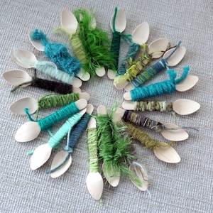 May include: A collection of wooden spoons wrapped with colourful yarn in shades of green, blue, and brown. The yarn is arranged in a circular pattern, creating a visually appealing and textured display.