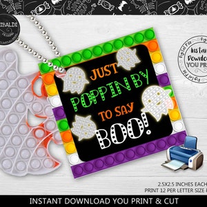 May include: A white ghost-shaped pop-it toy is attached to a tag that says "Just Poppin' By to Say Boo!" with ghost graphics. The tag has a colorful border and is connected to the toy with a silver chain. The image also includes a printer.