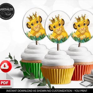 Op de afbeelding: Drie cupcake-toppers met een cartoon-leeuwenwelpje dat een gouden kroon draagt. Het leeuwenwelpje is omringd door groene bladeren. De toppers zijn op een witte achtergrond.