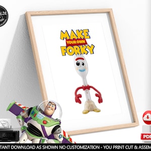 May include: A framed print featuring the text MAKE YOUR OWN FORKY in yellow and blue letters above an illustration of a white plastic spork character with red pipe cleaner arms, googly eyes, a blue mouth, and a tan clay base.