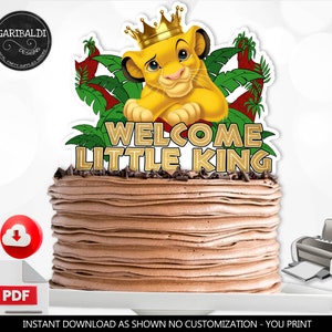 Op de afbeelding: Een printbare taarttopper met een cartoon leeuwenwelpje dat een gouden kroon draagt. Het leeuwenwelpje zit op een groene jungle achtergrond met de tekst "Welcome Little King" in gouden letters.