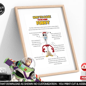 May include: A framed instructional print titled HOW TO MAKE YOUR OWN FORKY, featuring a step-by-step guide with text and arrows pointing to a white plastic spork character with googly eyes, red pipe cleaner arms, and a clay base.