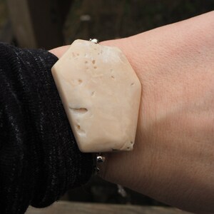 May include: A beige, irregularly shaped bracelet made of natural coral with a silver chain and clasp.