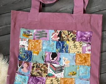 May include: A mauve tote bag with a patchwork design featuring various book-themed patterns. The patchwork includes images of books, flowers, and silhouettes. The bag has two long straps.