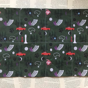 May include: Green fabric with a repeating pattern of red pickup trucks, white moons, black circles, paw prints, lavender sprigs, chains, and a sign that reads "The City of Twin Peaks, Washington".