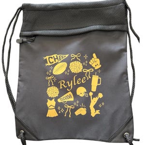May include: A black drawstring backpack featuring a mesh top panel and a yellow graphic print. The design includes the name Rylee surrounded by icons of a football, megaphone, pom-poms, cheer pennant, foam finger, tumbler, and a cheerleader.