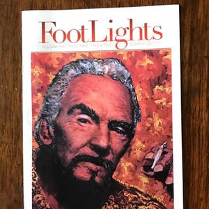 Può includere: Una copertina di rivista con un ritratto di Leon Katz, un uomo con barba e baffi bianchi, su uno sfondo rosso e arancione. La rivista è intitolata "FootLights: Illuminating the Theatre Community". Il testo "Leon Katz 1919-2017" è stampato sotto il ritratto. La copertina della rivista è firmata "Maris O'Dea | Hobbs 2017".