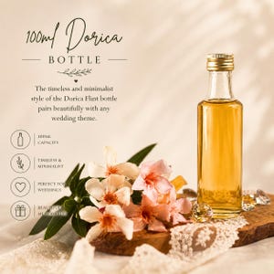 May include: A clear glass Dorica bottle with a gold cap, filled with a golden liquid, sits on a wooden board. The image includes text that reads "100ml Dorica Bottle". A bouquet of pink and white flowers and lace are also in the image.