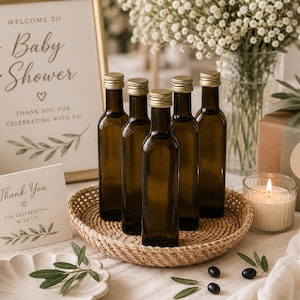 May include: A baby shower setup with olive oil bottles, a gift box, and a lit candle. A sign reads "Welcome to Baby Shower" and a card says "Thank You". The bottles are in a woven basket.