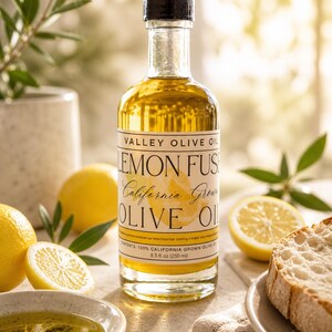 May include: A clear glass bottle of lemon-infused olive oil with a black cap, labeled "Valley Olive Oil Lemon Fuse California Grown Olive Oil." The bottle is surrounded by lemons, a small bowl of oil, and a slice of bread. The bottle contains 8.5 fl oz (250 ml).