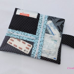 May include: A black fabric pouch with white polka dots featuring a light blue trim with a black branch pattern. The pouch has two zippered compartments, one with a clear plastic window, containing medical supplies like bandages and a blister pack.