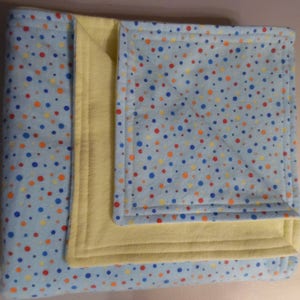 May include: A baby blanket with a light blue polka dot pattern in red, orange, and blue. The blanket has a yellow interior and is folded. The edges are stitched with a matching thread, creating a neat, finished look. This blanket is suitable for a baby.