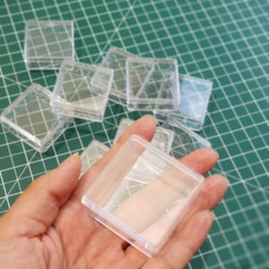 Peut inclure: Un ensemble de contenants carrés en plastique transparent, certains empilés les uns sur les autres. Les contenants sont petits et semblent destinés à contenir de petits objets.