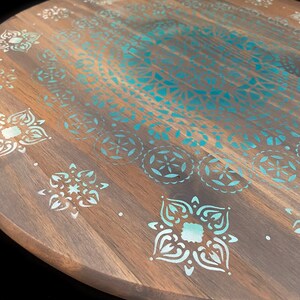 May include: A round wooden serving tray with a teal and white mandala design. The tray is painted with a soft gray base and an aqua ombre effect.