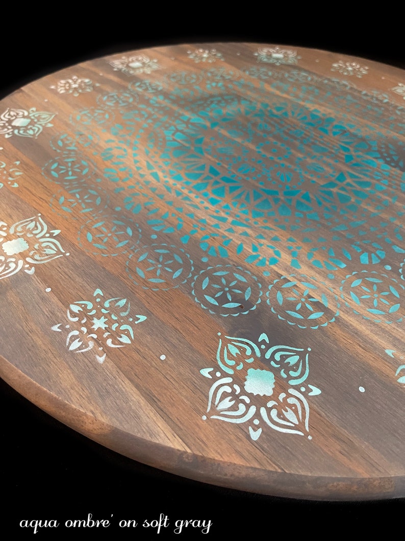 May include: A round wooden serving tray with a teal and white mandala design. The tray is painted with a soft gray base and an aqua ombre effect.