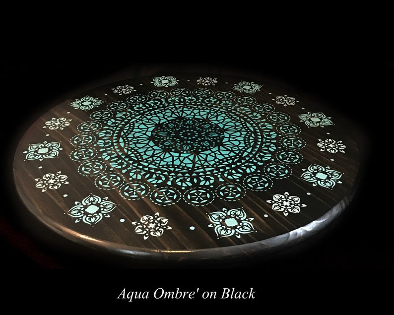 May include: A round wooden table top with a teal and black mandala design. The design features a large central mandala surrounded by smaller mandalas. The table top is painted black with a teal ombre effect.