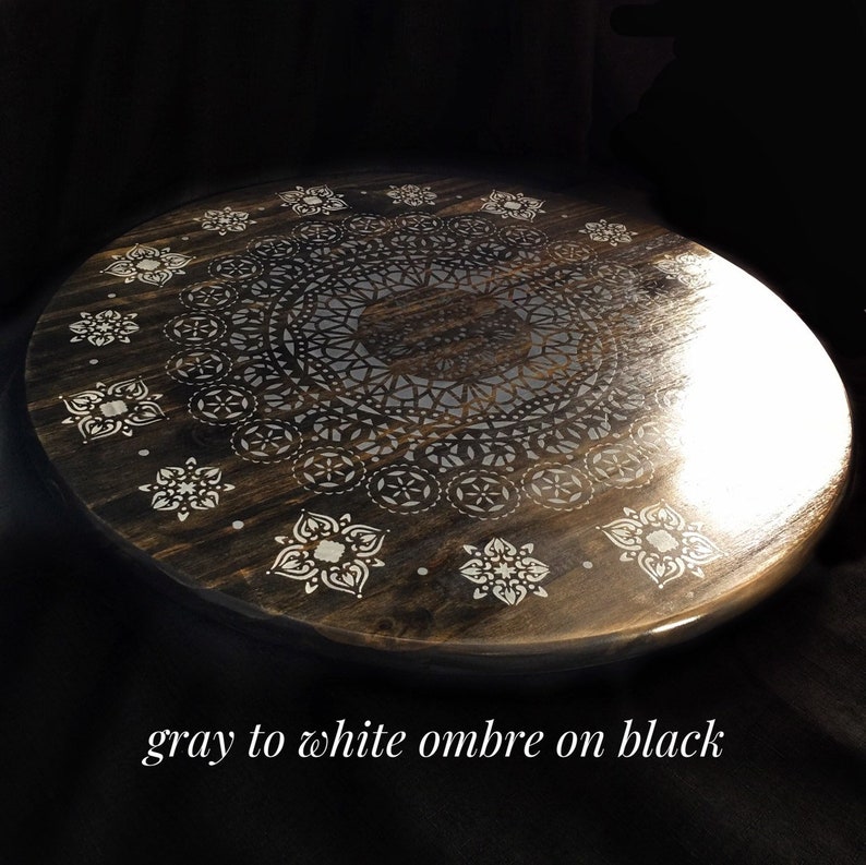 May include: A round wooden tray with a gray to white ombre paint finish and a black mandala design. The mandala is painted in a white stencil design.