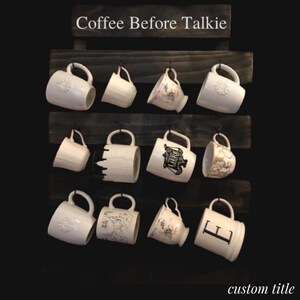 May include: A dark wood wall-mounted mug rack with three horizontal slats and metal hooks holding twelve assorted white ceramic mugs. The top slat features the white text Coffee Before Talkie. The bottom right corner displays the text custom title.