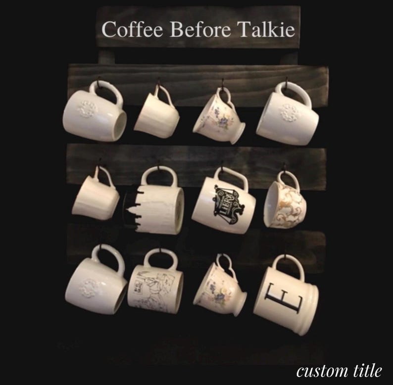May include: A dark wood wall-mounted mug rack with three horizontal slats and metal hooks holding twelve assorted white ceramic mugs. The top slat features the white text Coffee Before Talkie. The bottom right corner displays the text custom title.