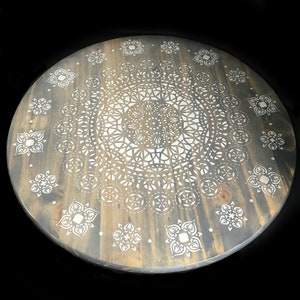May include: A round wooden table top with a gray stain and a white mandala design painted on the surface.