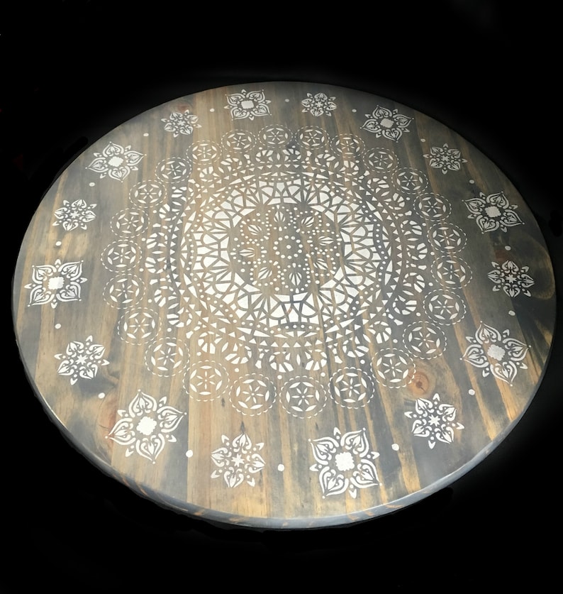 May include: A round wooden table top with a gray stain and a white mandala design painted on the surface.