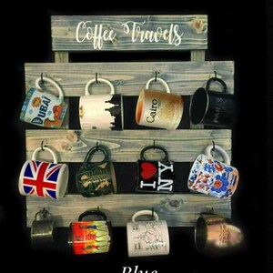 May include: A blue-toned wooden wall-mounted mug rack with the text Coffee Travels printed at the top. The rack features three horizontal slats with twelve black metal hooks, each holding a ceramic mug with various travel-themed designs.