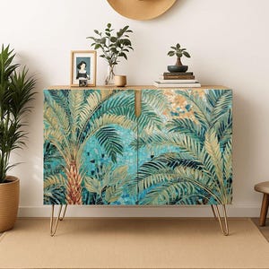 May include: A wooden cabinet with a tropical palm tree design. The cabinet has a light wood top and gold hairpin legs. The doors feature a mosaic-style illustration of palm trees in shades of green and blue. A straw hat hangs above the cabinet.