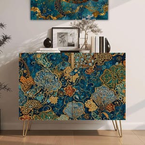 May include: A rectangular cabinet with two doors featuring a deep blue and gold floral pattern, supported by four thin gold metal legs. The cabinet surface displays intricate botanical motifs in shades of teal, navy, and metallic gold.