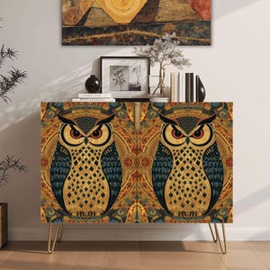 May include: A rectangular cabinet with gold-toned metal hairpin legs, featuring a repeating pattern of two large owls with orange eyes and intricate gold, black, and blue geometric plumage on the front doors.