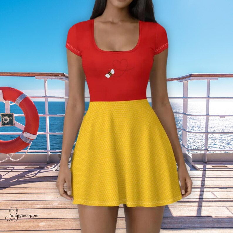 May include: A red and yellow skater dress. The top is red with a small bee graphic. The skirt is yellow with a small dot pattern. The dress has a scoop neckline and short sleeves. The dress is worn on a wooden deck with a life preserver and the ocean in the background.