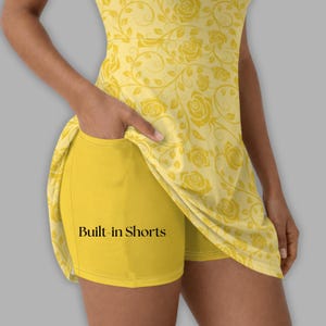 May include: Yellow athletic dress with built-in shorts. The dress features a floral rose pattern and the text "Built-in Shorts" on the shorts. The dress is sleeveless and has a scoop neckline. The shorts are a solid yellow color.