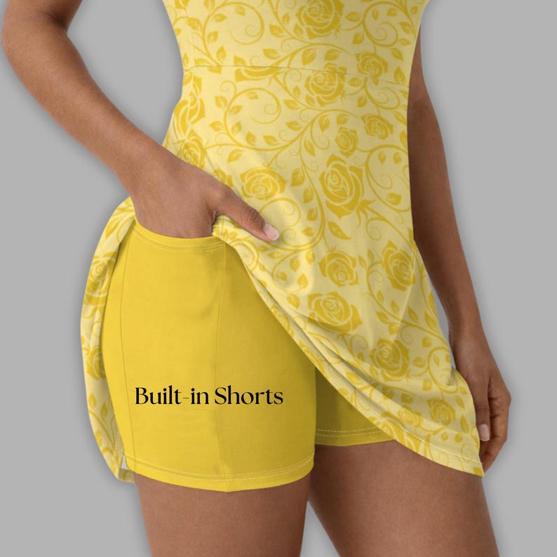 May include: Yellow athletic dress with built-in shorts. The dress features a floral rose pattern and the text "Built-in Shorts" on the shorts. The dress is sleeveless and has a scoop neckline. The shorts are a solid yellow color.