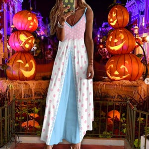 May include: A sleeveless maxi dress with a V-neckline, featuring a white bodice with pink polka dots and a light blue skirt. The dress has a decorative trim and is set against a Halloween-themed background with carved pumpkins.