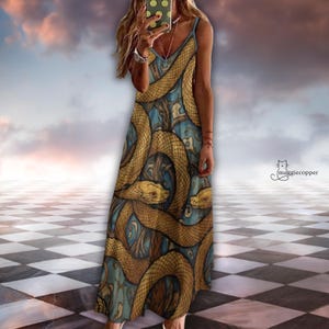 May include: A long, flowing dress with a V-neck and spaghetti straps. The dress features a repeating pattern of golden-brown snakes on a teal and blue background. The dress is floor-length and appears to be made of a lightweight fabric.
