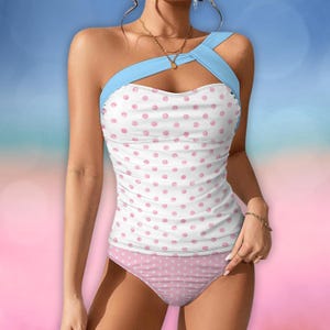 Könnte beinhalten: Ein weißer Badeanzug mit rosa Punkten und einem hellblauen Träger. Der Badeanzug hat einen Tanktop-Stil mit passendem Unterteil. Die Punkte sind in einem zarten Rosa gehalten.