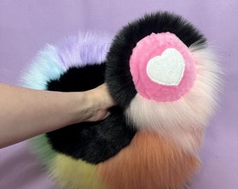 May include: A colourful faux fur tail with a pink heart patch. The tail is made of different colours of fur, including black, white, light blue, lavender, yellow and orange.