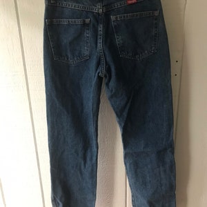 May include: A pair of blue denim jeans with a brown leather Wrangler label on the back pocket.