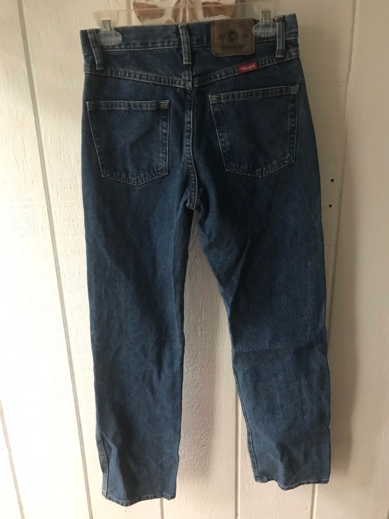 May include: A pair of blue denim jeans with a brown leather Wrangler label on the back pocket.