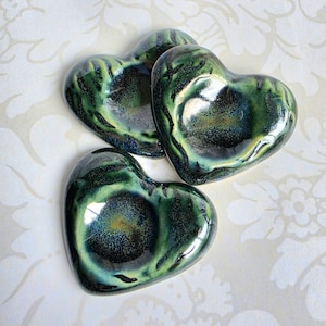 May include: Three heart-shaped ceramic objects with a glossy finish. The glaze features a blend of deep forest green, dark navy blue, and black tones, creating a marbled effect with lighter green highlights along the edges of each piece.