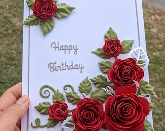 Może przedstawiać: Biała kartka z napisem "Happy Birthday" w szarym kolorze. Kartka jest ozdobiona czerwonymi papierowymi różami i zielonymi liśćmi.