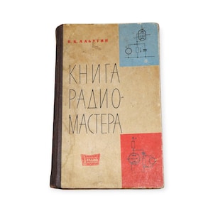 May include: Vintage book titled "KNIGA RADIO MASTERA" in Russian. The cover is tan with black text and illustrations in blue and red. The book has a worn appearance, suggesting age and use.