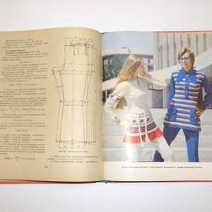 Pode incluir: Um livro aberto com um padrão de costura na página esquerda e uma foto de duas mulheres vestindo roupas diferentes na página direita. O texto na página esquerda está em russo. O texto na página direita diz "Vestido de malha azul listrado com acabamento decorativo, calças de malha marrom listradas."