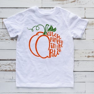 May include: White t-shirt with a pumpkin design and the text "Cutest Pumpkin in the Patch".
