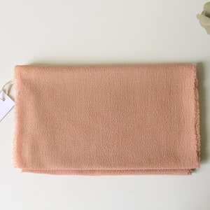 May include: A pale pink fabric swatch with a frayed edge. The fabric has a subtle texture. A white tag with the text "aroma 30" is attached to the fabric.