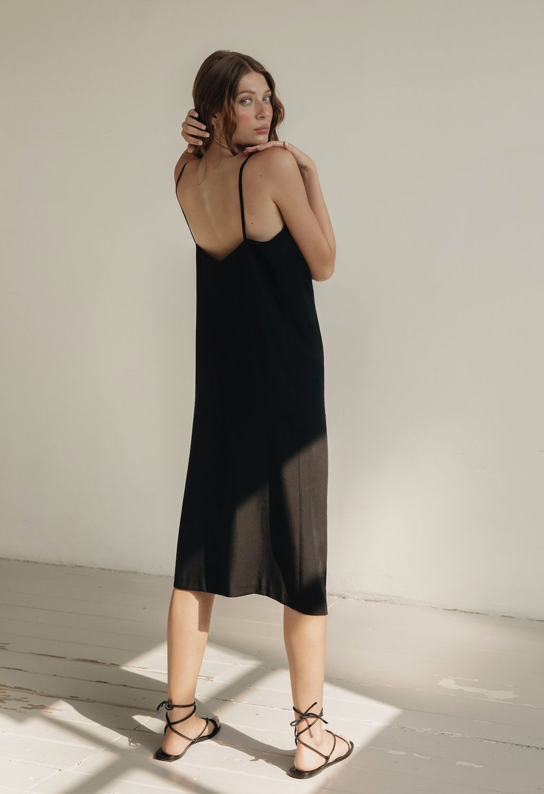 K&ouml;nnte beinhalten: Schwarzes Slip-Kleid mit d&uuml;nnen Spaghettitr&auml;gern. Das Kleid reicht bis zur Mitte der Wade. Das Model tr&auml;gt schwarze Riemchensandalen. Der Hintergrund ist neutral.