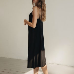 K&ouml;nnte beinhalten: Ein schwarzes Midikleid mit Spaghettitr&auml;gern. Das Kleid wird mit schwarzen Riemchensandalen kombiniert. Der Hintergrund ist ein Raum mit wei&szlig;en W&auml;nden und Holzboden.
