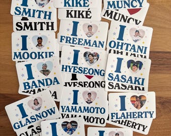 May include: A selection of white square stickers with a blue "I" and a heart-shaped photo. Each sticker displays a different name, including "Smith," "Kike," and "Muncy," with the name repeated below. The stickers have a baseball theme.
