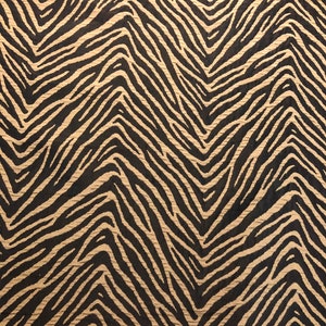 May include: A fabric with a black and tan chevron pattern. The pattern resembles a zebra print.