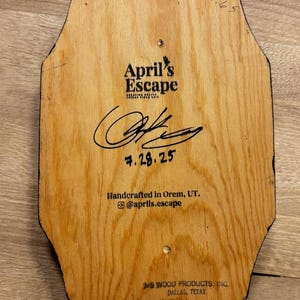 May include: Wooden plaque with the text "April's Escape" and a signature. The plaque is handcrafted in Orem, UT, and includes the date 7.28.25. The bottom of the plaque reads "J.S. Wood Products, Inc., Dallas, Texas."